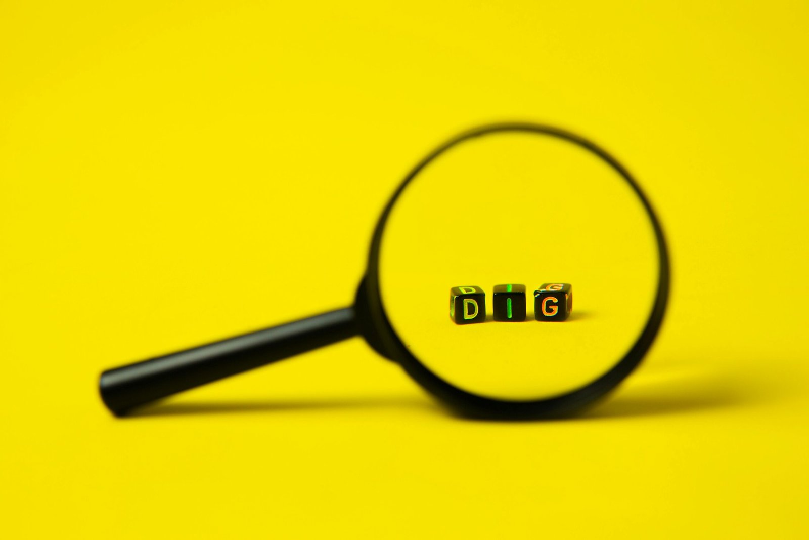 Background of big black magnifier with word dig in form of cubes against yellow surface